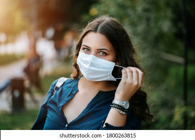 Young brunette beautiful women in city street or park weared with face mask that protect against the spread of corona virus disease or SARS-CoV-2. Social distancing during pandemic COVID 19.