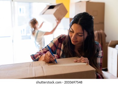 Young Brunette Caucasian Woman Writes Label On Cardboard Box For House Move. Copy Space. Relocation Concept.