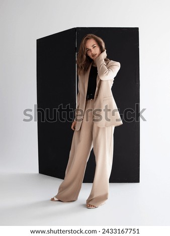 Young brunette curly woman in beige suit. Elegant style. A beautiful fashion model poses in a loose beige pantsuit. Female fashion. Full-length studio portrait.