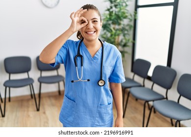 Young Brunette Doctor Woman At Waiting Room Smiling Happy Doing Ok Sign With Hand On Eye Looking Through Fingers 