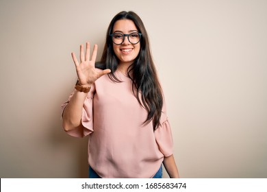 Young brunette elegant woman wearing glasses over isolated background showing and pointing up with fingers number five while smiling confident and happy.