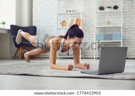 Young brunette exercising at home watching fitness training video on laptop computer. Side view.