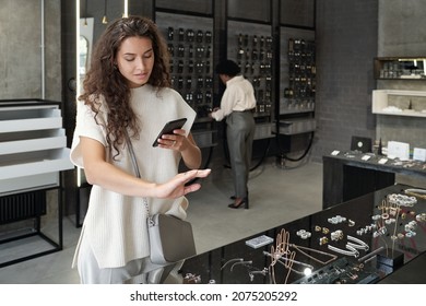 Young brunette female consumer trying on ring and photographing it while choosing rings in contemporary jewelry shop - Powered by Shutterstock