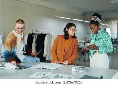 Young brunette female fashion designer looking at screen of tablet held by African American woman during presentation of new items - Powered by Shutterstock