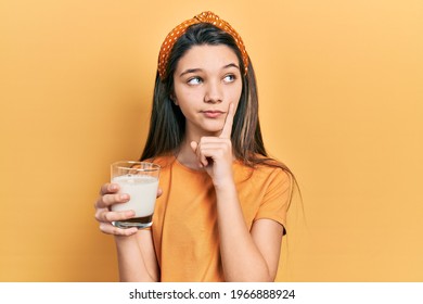 Young Brunette Girl Drinking A Glass Of Milk Serious Face Thinking About Question With Hand On Chin, Thoughtful About Confusing Idea 