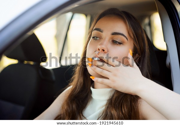 Young brunette girl\
driving the car and smoking cigarette. Dangerous bold driving,\
breaking the rule,\
close-up.