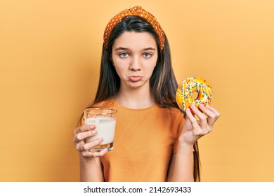 Young Brunette Girl Eating Donut And Drinking Glass Of Milk Depressed And Worry For Distress, Crying Angry And Afraid. Sad Expression. 