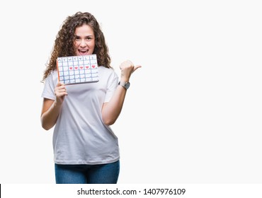 Young Brunette Girl Holding Menstruation Calendar Over Isolated Background Pointing And Showing With Thumb Up To The Side With Happy Face Smiling