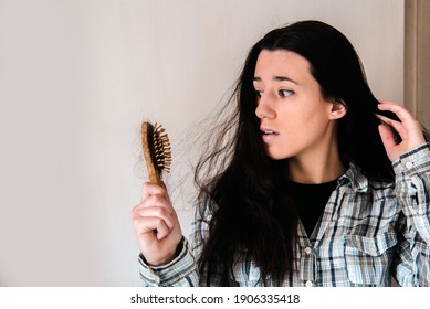 Young brunette girl holds a comb with hair falling out in her hand, looks worried and frustrated