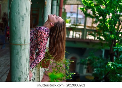 Young brunette girl with long hair and head thrown back on the wooden balcony in an old house