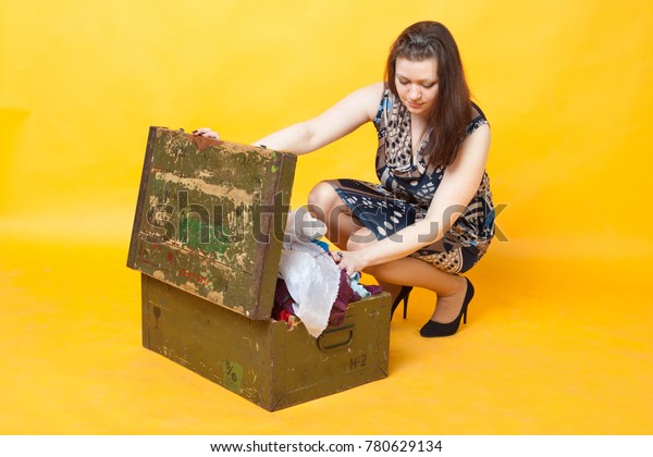 young brunette girl puts away things in a\
wooden box, on yellow\
background