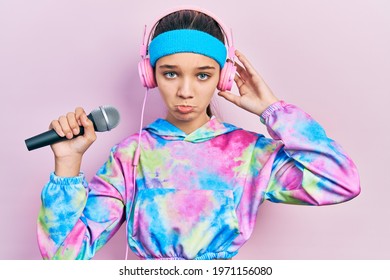 Young Brunette Girl Singing Song Using Microphone Wearing Sportswear Depressed And Worry For Distress, Crying Angry And Afraid. Sad Expression. 