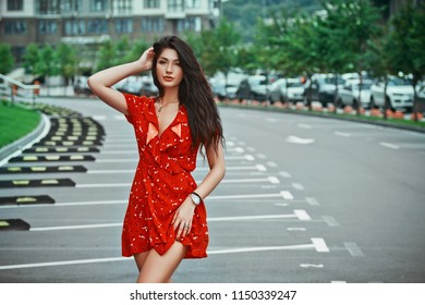 Young Brunette Girl Standing And Poses In Red Short Dressn The City Street, Walking On Empty Parking Place