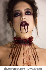 young brunette girl with stylish dark make-up with the blood that flows from her neck and mouth, halloween concept