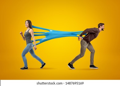 Young brunette girl wearing casual jeans and t-shirt stuck to young man in casual clothes with blue sticky slime on yellow background. People and objects. People and relationship. Feelings and