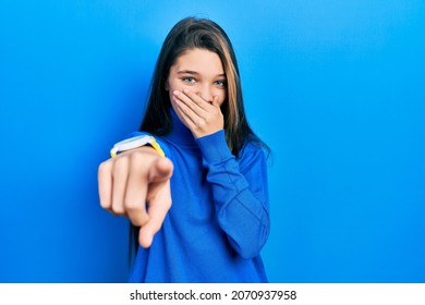 Young Brunette Girl Wearing Turtleneck Sweater Laughing At You, Pointing Finger To The Camera With Hand Over Mouth, Shame Expression 