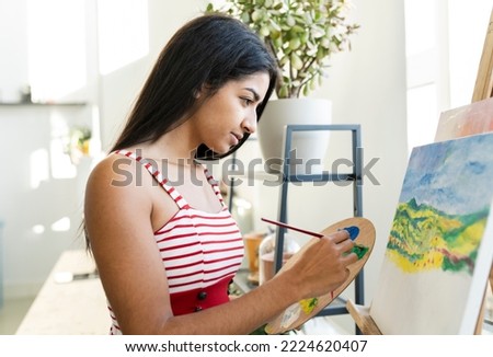 Young brunette hindu woman painting a oil paint picture at home. Millennial indian female at home.