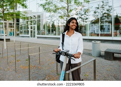 Young Brunette Indian Woman Smiling While Riding Electric Scooter On City Street