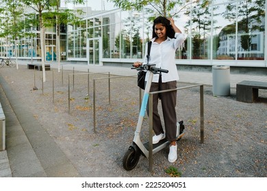 Young Brunette Indian Woman Smiling While Riding Electric Scooter On City Street