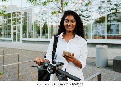 Young Brunette Indian Woman Using Cellphone While Riding Electric Scooter On City Street