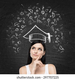 Young brunette lady is thinking about studying at the university. Educational icons are drawn on the black chalk board. - Powered by Shutterstock