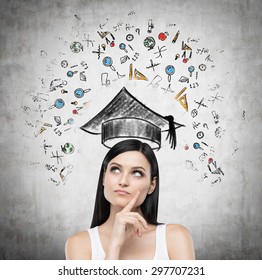 Young brunette lady is thinking about studying at the university. Educational icons are drawn on concrete wall. - Powered by Shutterstock