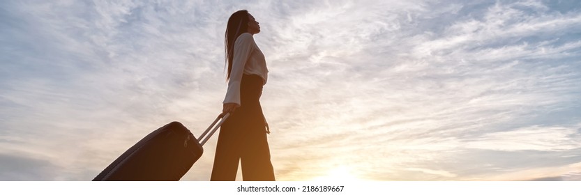 Young Brunette With Long Hair In Businesswear On High Heels Walks Pulling Black Suitcase. Woman Goes On Road Against Cloudy Sky Low Angle Shot, Sinlight