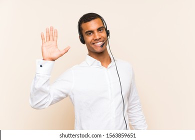 Young brunette man working with a headset saluting with hand with happy expression