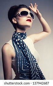 Young Brunette Model Wearing A Sunglasses And A Scarf Posing On Gray Background