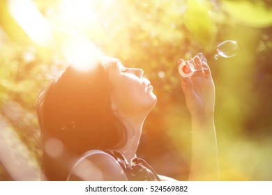 Young brunette stands in the bushes and inflate bubbles. Bright sunny day. - Powered by Shutterstock