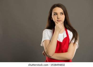 Young brunette supermarket employee thinking wearing a red apron - Powered by Shutterstock