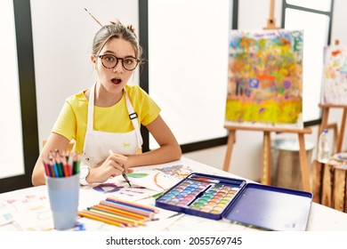 Young Brunette Teenager At Art Studio In Shock Face, Looking Skeptical And Sarcastic, Surprised With Open Mouth 