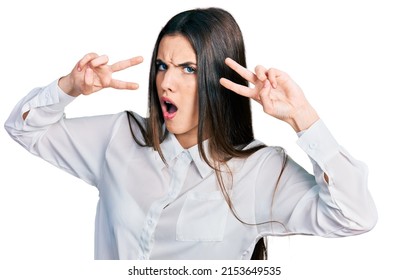 Young Brunette Teenager Doing Peace Gesture Close To Eyes In Shock Face, Looking Skeptical And Sarcastic, Surprised With Open Mouth 