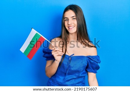 Young brunette teenager holding bulgaria flag looking positive and happy standing and smiling with a confident smile showing teeth 