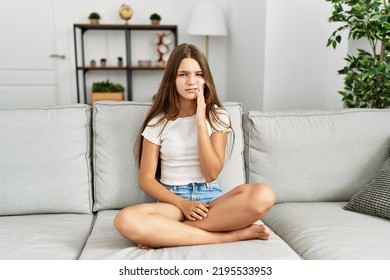 Young brunette teenager sitting on the sofa at home touching mouth with hand with painful expression because of toothache or dental illness on teeth. dentist  - Shutterstock ID 2195533953