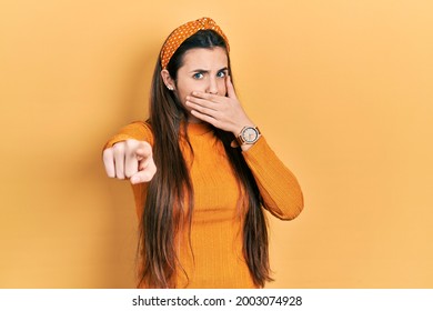 Young Brunette Teenager Wearing Casual Yellow Sweater Laughing At You, Pointing Finger To The Camera With Hand Over Mouth, Shame Expression 