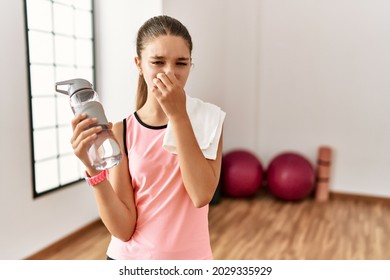 Young Brunette Teenager Wearing Sportswear Holding Water Bottle Smelling Something Stinky And Disgusting, Intolerable Smell, Holding Breath With Fingers On Nose. Bad Smell 