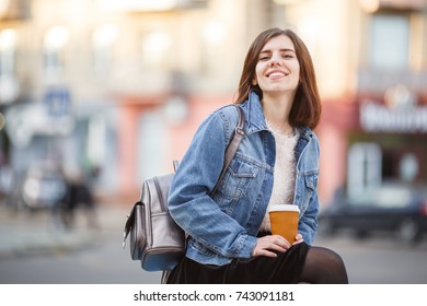 Young brunette is walking down the street with coffee and laughing.