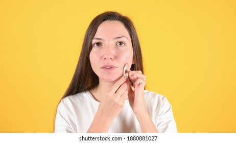 Young brunette who checks her skin on yellow background. Cosmetology, skin care, acne treatment.