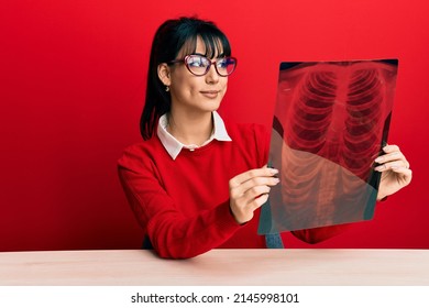 Young Brunette Woman With Bangs Holding Chest Radiography Smiling Looking To The Side And Staring Away Thinking. 