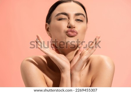 young and brunette woman with bare shoulders pouting lips isolated on pink