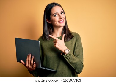 Young Brunette Woman With Blue Eyes Working Using Computer Laptop Over Yellow Background Cheerful With A Smile On Face Pointing With Hand And Finger Up To The Side With Happy And Natural Expression