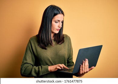 Young brunette woman with blue eyes working using computer laptop over yellow background Checking the time on wrist watch, relaxed and confident