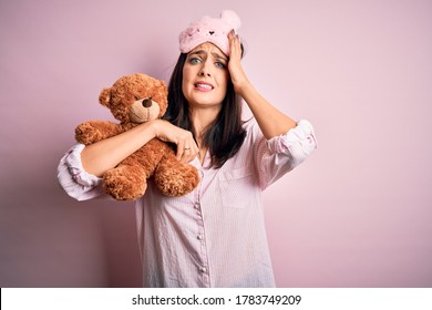 Young Brunette Woman With Blue Eyes Wearing Pajama Hugging Teddy Bear Stuffed Animal Stressed With Hand On Head, Shocked With Shame And Surprise Face, Angry And Frustrated. Fear And Upset For Mistake.