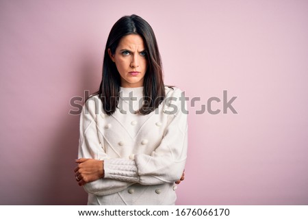 Young brunette woman with blue eyes wearing casual sweater over isolated pink background skeptic and nervous, disapproving expression on face with crossed arms. Negative person.