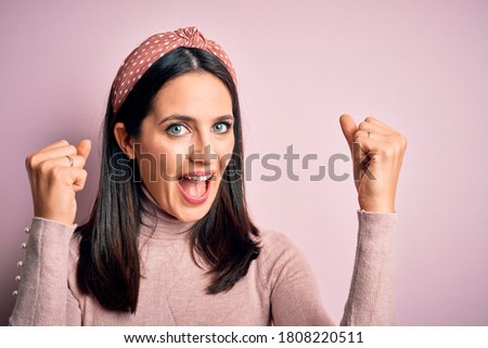 Young brunette woman with blue eyes wearing casual t-shirt and diadem celebrating surprised and amazed for success with arms raised and open eyes. Winner concept.