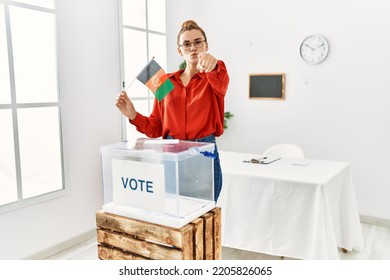 Young Brunette Woman By Ballot Box Holding Afghanistan Flag Pointing With Finger To The Camera And To You, Confident Gesture Looking Serious 