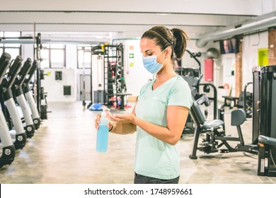 Young brunette woman cleans her hands with an antibacterial gel at the gym. She's wearing a mask. - Powered by Shutterstock