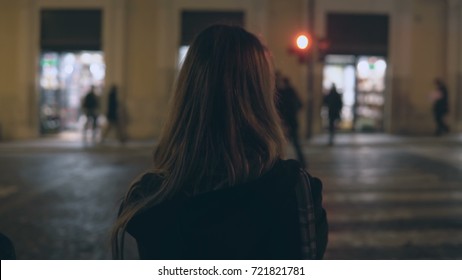 Young brunette woman crossing the traffic road in the evening and walking in the city centre alone, through the streets.