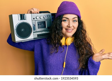 Young brunette woman with curly hair holding boombox, listening to music celebrating achievement with happy smile and winner expression with raised hand  - Shutterstock ID 1923534593